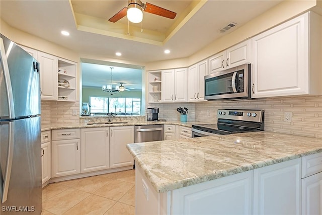 kitchen featuring a raised ceiling, white cabinetry, appliances with stainless steel finishes, and light stone counters