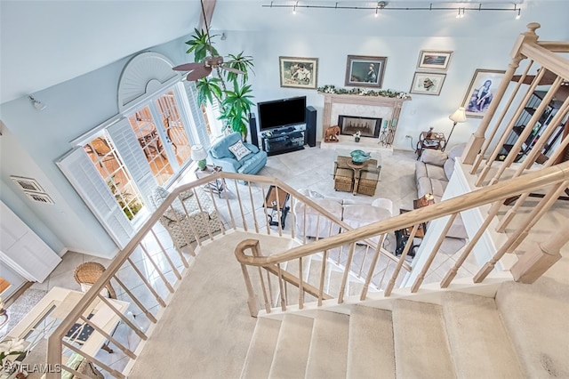 staircase featuring rail lighting, lofted ceiling, and a high end fireplace