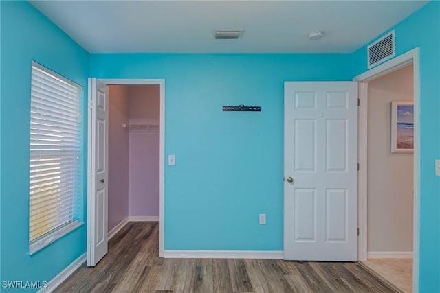 unfurnished bedroom featuring wood-type flooring, a spacious closet, and a closet