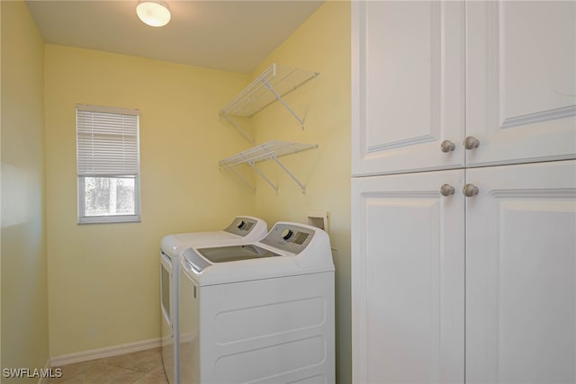 clothes washing area with cabinets, washing machine and clothes dryer, and light tile patterned floors