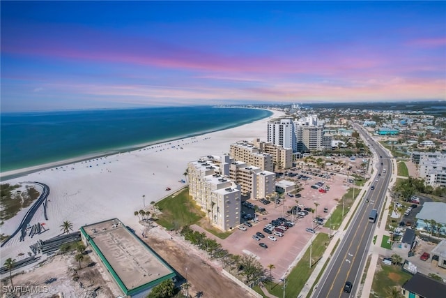 aerial view at dusk with a water view and a beach view