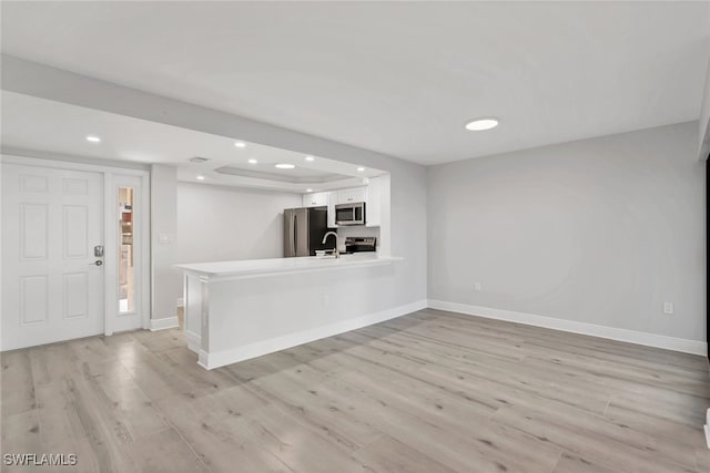 interior space featuring appliances with stainless steel finishes, kitchen peninsula, light hardwood / wood-style floors, and white cabinets