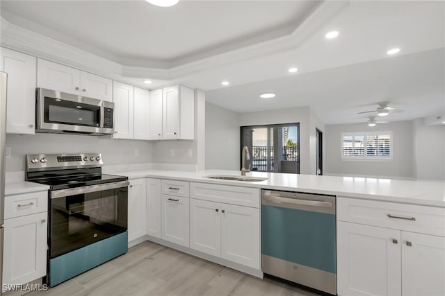 kitchen featuring sink, light hardwood / wood-style flooring, kitchen peninsula, stainless steel appliances, and white cabinets