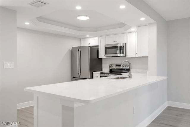 kitchen featuring appliances with stainless steel finishes, kitchen peninsula, a raised ceiling, light hardwood / wood-style floors, and white cabinets