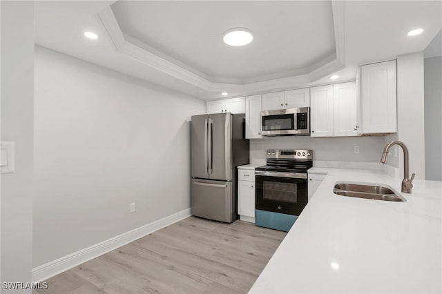 kitchen with a raised ceiling, sink, white cabinets, stainless steel appliances, and light wood-type flooring