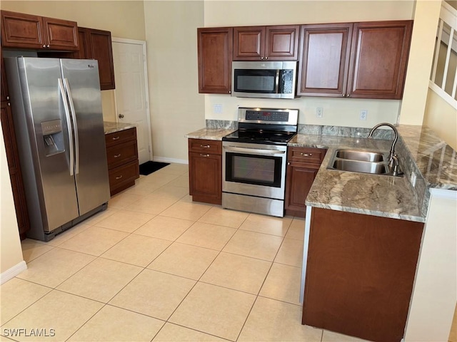 kitchen with appliances with stainless steel finishes, stone countertops, sink, light tile patterned floors, and kitchen peninsula