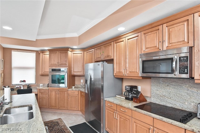 kitchen with sink, light stone counters, crown molding, appliances with stainless steel finishes, and a tray ceiling