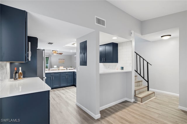 kitchen featuring stainless steel fridge, decorative backsplash, ceiling fan, blue cabinetry, and light wood-type flooring