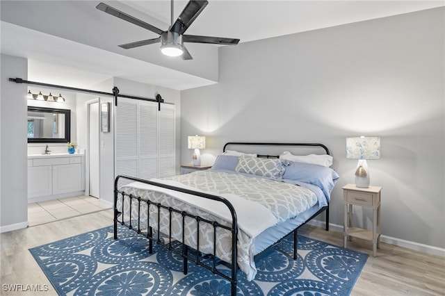 bedroom with ensuite bathroom, sink, ceiling fan, a barn door, and light hardwood / wood-style floors