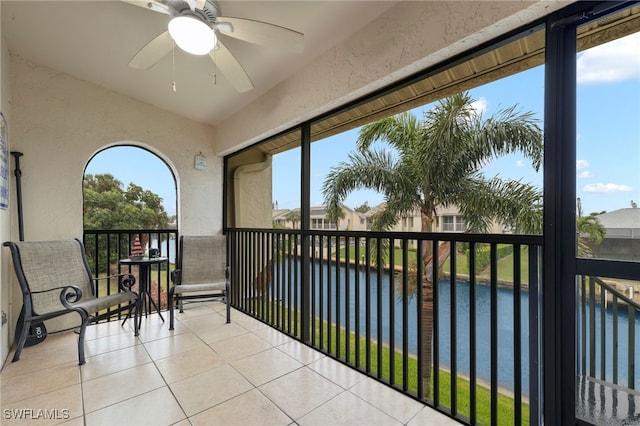 sunroom with ceiling fan and a water view