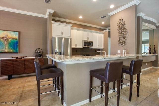 kitchen featuring appliances with stainless steel finishes, light stone countertops, a breakfast bar area, and white cabinets