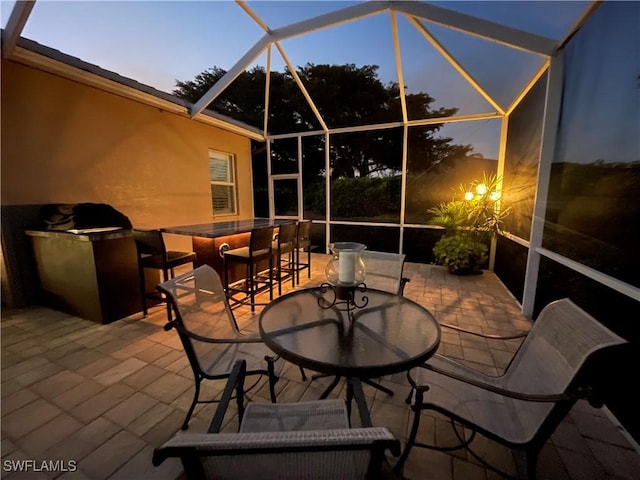 patio terrace at dusk featuring an outdoor bar and glass enclosure