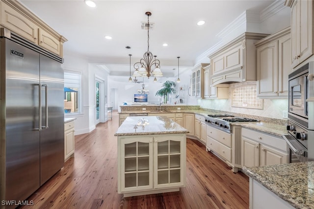 kitchen featuring built in appliances, a center island, hanging light fixtures, ornamental molding, and cream cabinetry