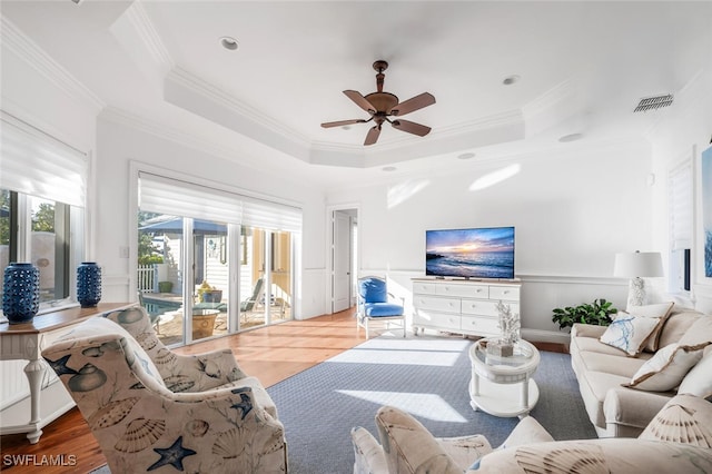 living room featuring hardwood / wood-style flooring, crown molding, ceiling fan, and a tray ceiling