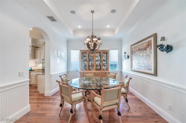 dining room with light hardwood / wood-style flooring, ornamental molding, a raised ceiling, and a chandelier