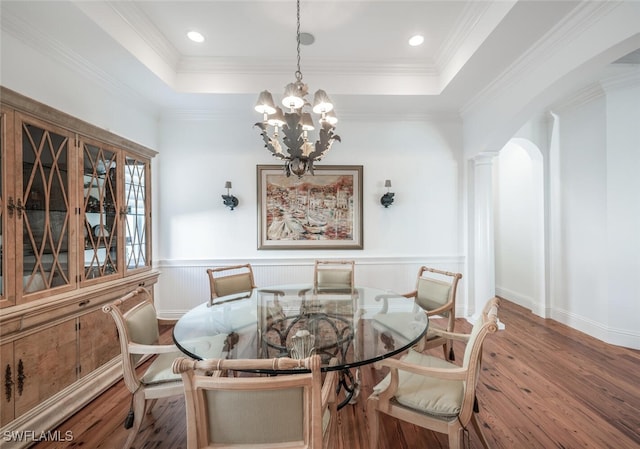 dining area with a raised ceiling, crown molding, hardwood / wood-style floors, and a notable chandelier