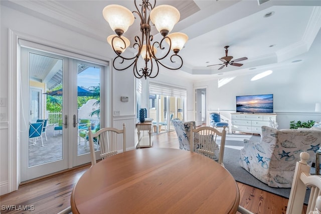 dining room with light hardwood / wood-style floors, ornamental molding, french doors, ceiling fan with notable chandelier, and a raised ceiling