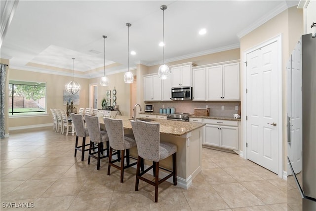 kitchen featuring appliances with stainless steel finishes, white cabinets, decorative light fixtures, and an island with sink