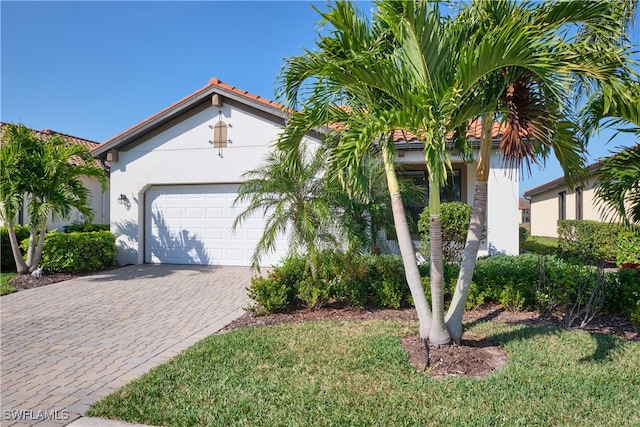 view of front of house featuring a garage, a tile roof, decorative driveway, stucco siding, and a front lawn