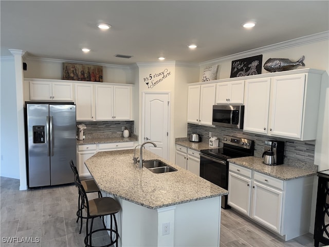 kitchen featuring appliances with stainless steel finishes, white cabinetry, an island with sink, sink, and light stone counters