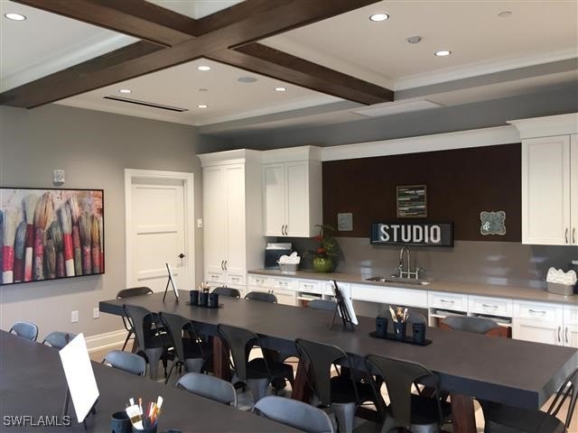 kitchen with beamed ceiling, white cabinetry, and sink