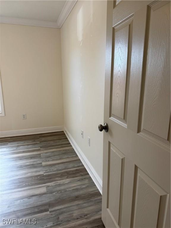 empty room with ornamental molding, baseboards, and dark wood-style floors