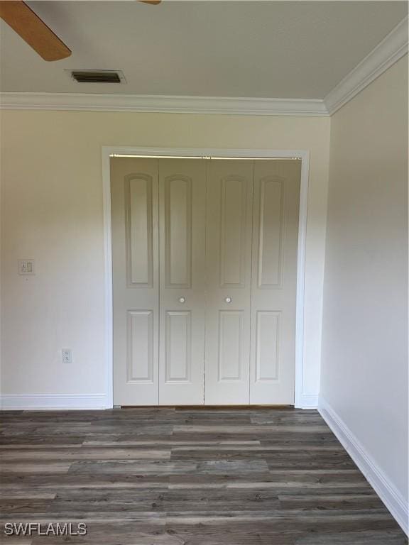 unfurnished bedroom with dark wood-style flooring, a closet, visible vents, ornamental molding, and baseboards