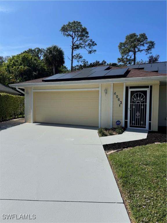 ranch-style home featuring driveway, an attached garage, and solar panels