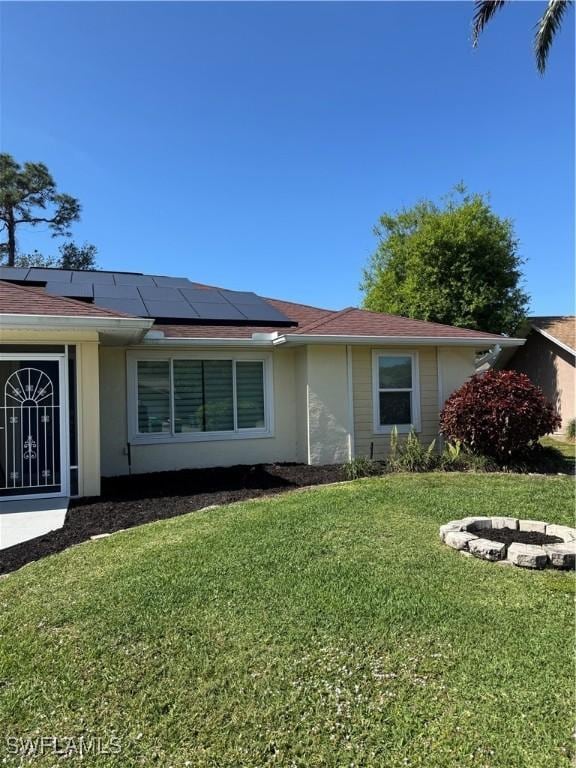 ranch-style house featuring a front lawn, stucco siding, and roof mounted solar panels