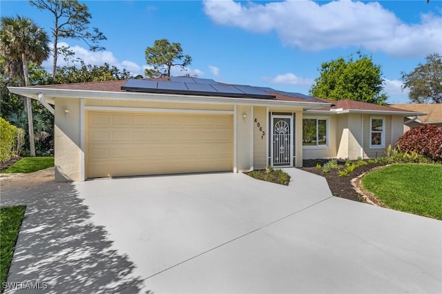 ranch-style home featuring a garage, driveway, solar panels, and stucco siding