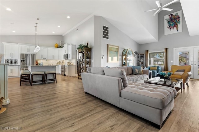 living room with high vaulted ceiling, sink, ceiling fan, light hardwood / wood-style floors, and french doors