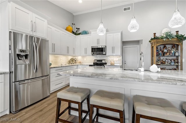 kitchen featuring a breakfast bar, white cabinetry, light stone counters, decorative light fixtures, and appliances with stainless steel finishes