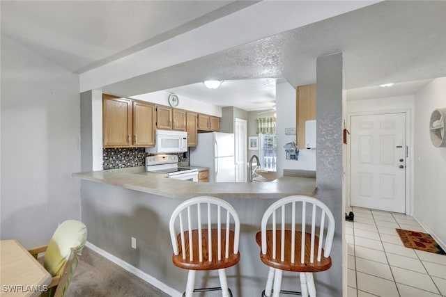 kitchen featuring a breakfast bar, sink, backsplash, kitchen peninsula, and white appliances