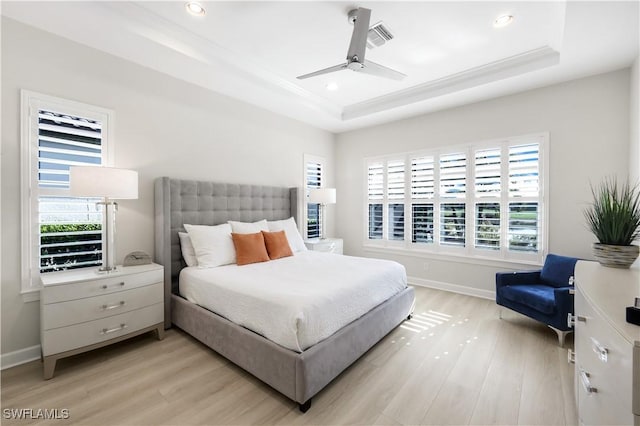 bedroom featuring multiple windows, light wood-type flooring, and a tray ceiling