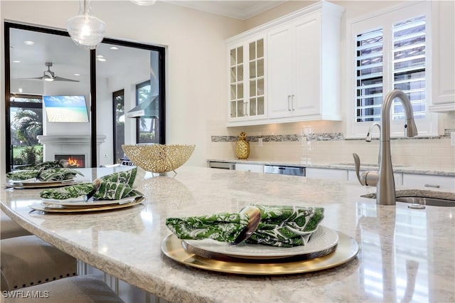 kitchen with sink, hanging light fixtures, light stone countertops, a large fireplace, and white cabinets