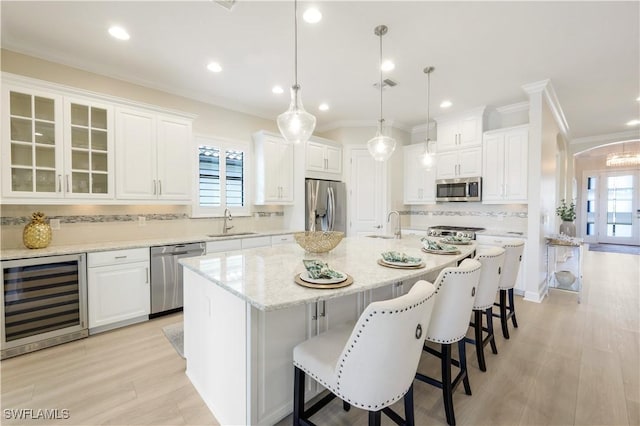 kitchen featuring wine cooler, white cabinetry, hanging light fixtures, stainless steel appliances, and a kitchen island with sink