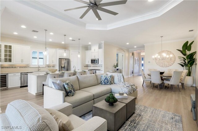 living room with sink, a tray ceiling, ornamental molding, light hardwood / wood-style floors, and beverage cooler