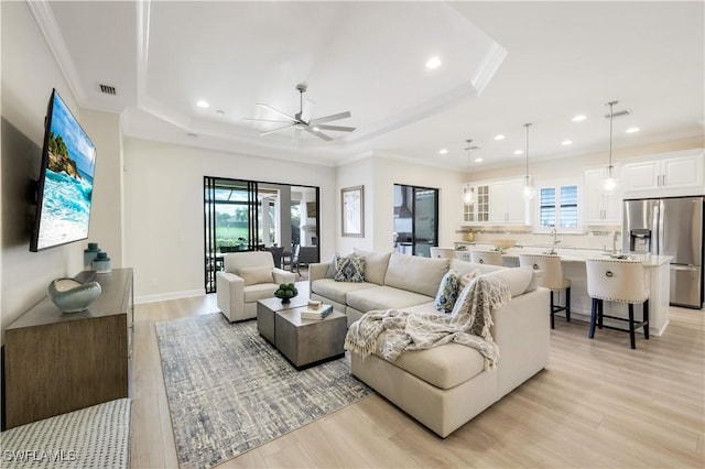 living room featuring crown molding, ceiling fan, light hardwood / wood-style floors, and a tray ceiling