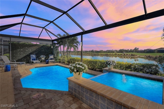 pool at dusk with a patio, a water view, and a lanai