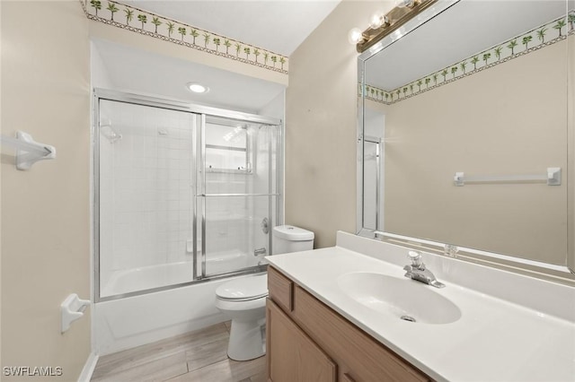 full bathroom featuring vanity, wood-type flooring, bath / shower combo with glass door, and toilet