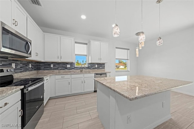 kitchen with white cabinetry, stainless steel appliances, decorative light fixtures, and a center island