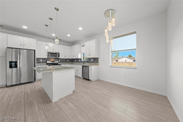 kitchen with appliances with stainless steel finishes, a center island, white cabinets, and decorative light fixtures