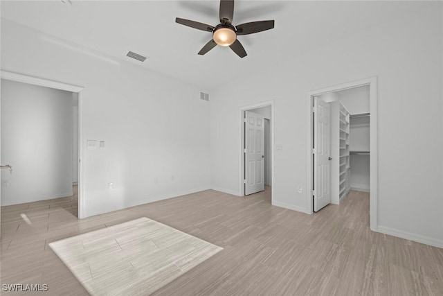 unfurnished bedroom featuring ceiling fan, a walk in closet, a closet, and light hardwood / wood-style flooring