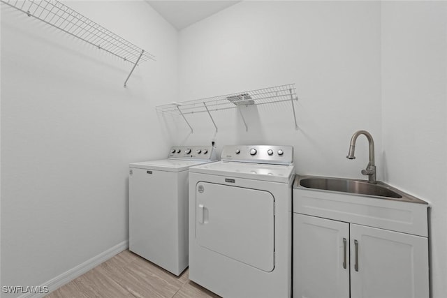 laundry area featuring cabinets, sink, washing machine and dryer, and light hardwood / wood-style flooring