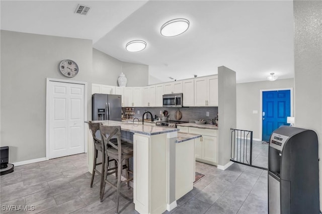 kitchen featuring appliances with stainless steel finishes, a kitchen island with sink, white cabinets, and a kitchen bar