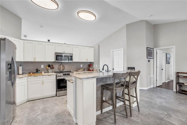 kitchen featuring white cabinetry, lofted ceiling, stainless steel appliances, and a center island with sink