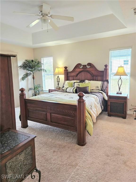 carpeted bedroom featuring ceiling fan and a tray ceiling