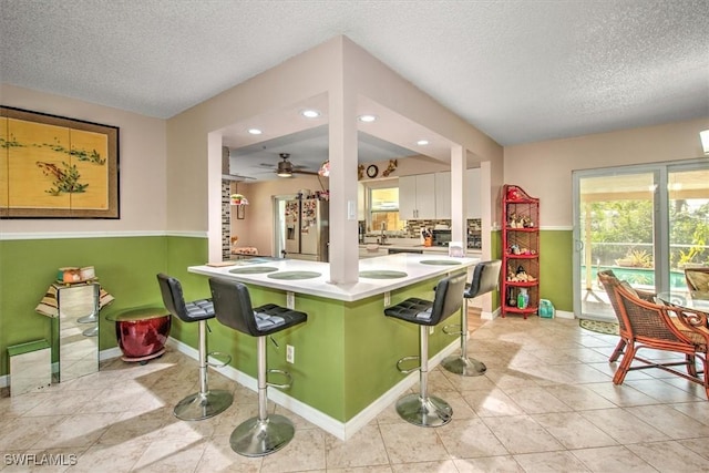 kitchen with white cabinetry, stainless steel fridge, a breakfast bar, and kitchen peninsula