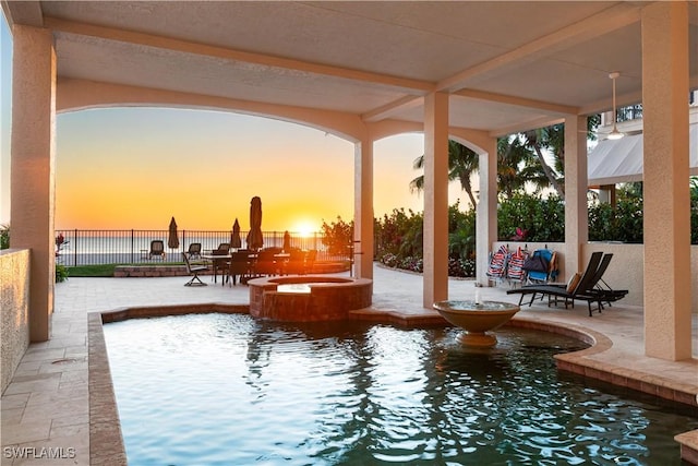 pool at dusk featuring a water view and a patio