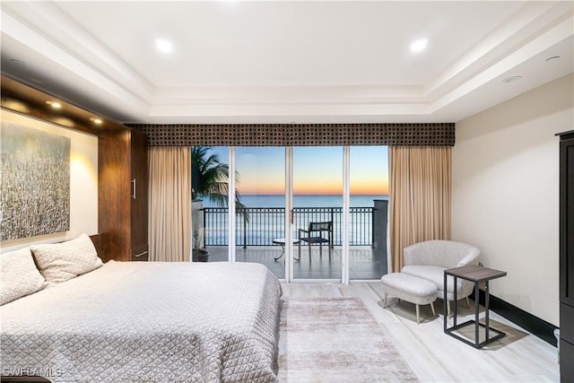 bedroom featuring a tray ceiling, access to outside, wood-type flooring, and a water view